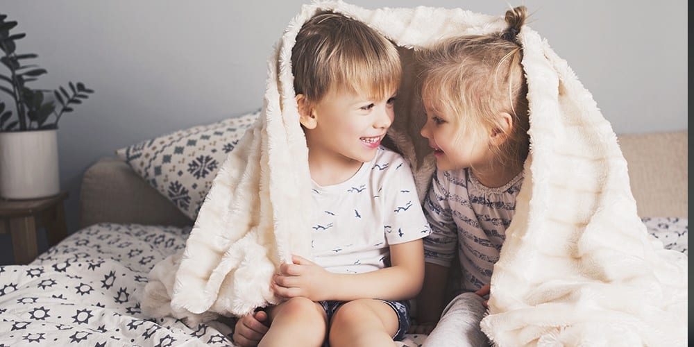 child siblings smiling and wrapped in a blanket